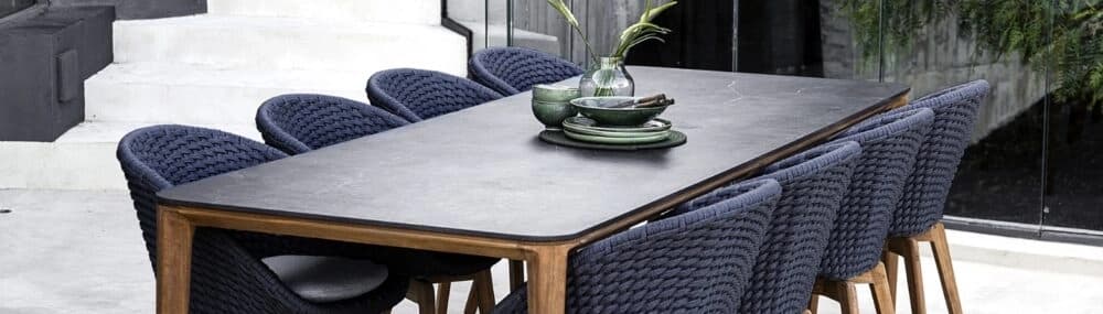 Modern outdoor dining table with a dark tabletop and woven navy dining chairs, styled with tableware and greenery in a contemporary patio setting.