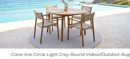 A round wooden table and woven chairs sit on a grey circular rug beside a pool. Image Text: Cane-line Circle Light Grey Round Indoor/Outdoor Rug