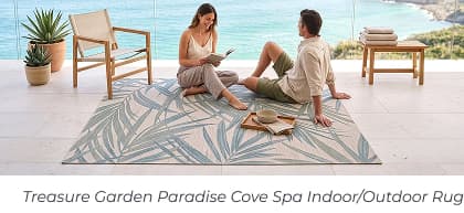 A couple relaxes together on a light-colored rug with a blue palm leaf print by the sea. Image Text: Treasure Garden Paradise Cove Spa Indoor/Outdoor Rug