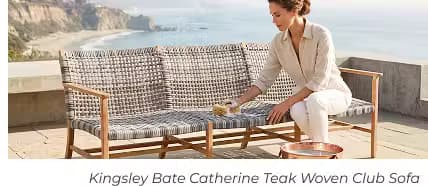 Woman cleaning a woven teak outdoor sofa on a coastal patio with ocean views and a copper bowl beside the seating.