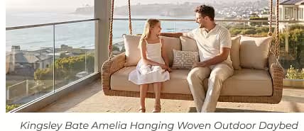 Man and young girl sitting together on a hanging woven outdoor daybed with glass railing and panoramic ocean views. (