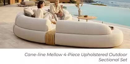 Two people sit on a curved upholstered outdoor sectional beside an infinity pool with coastal ocean views.