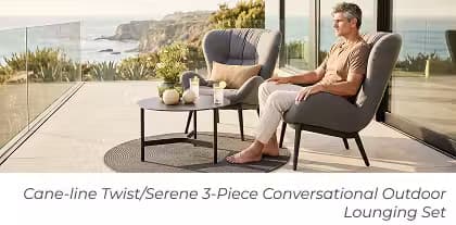Man relaxes in a cushioned lounge chair beside a round coffee table on a modern oceanfront patio.