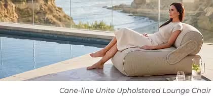Woman relaxing in a Cane-line Unite upholstered lounge chair beside an infinity pool overlooking the ocean.