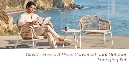 Man reading in a woven outdoor conversation set with ocean views and a modern side table.