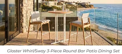 Two bar-height chairs and a round table on a coastal balcony overlooking the beach.