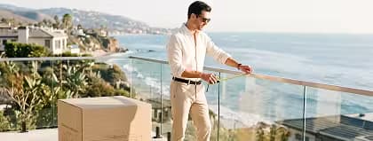 Man measuring a glass balcony railing on a coastal terrace beside a boxed outdoor furniture delivery.