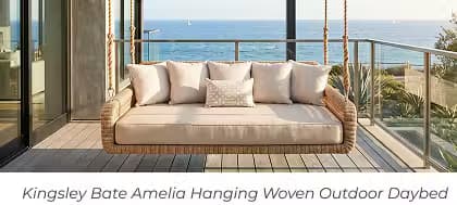 Woven hanging outdoor daybed with plush cushions suspended on a coastal balcony overlooking the ocean.