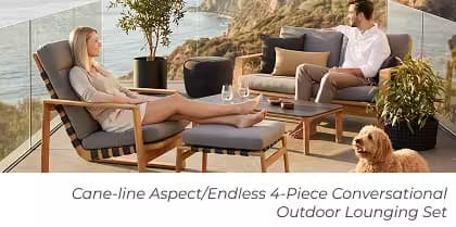 Couple relaxing in a modern outdoor lounge with cushioned seating, ottoman, dog, and coastal views.
